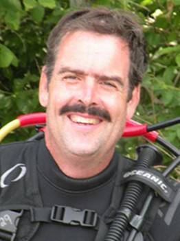 Tim Green in scuba suit smiling in front of a tree